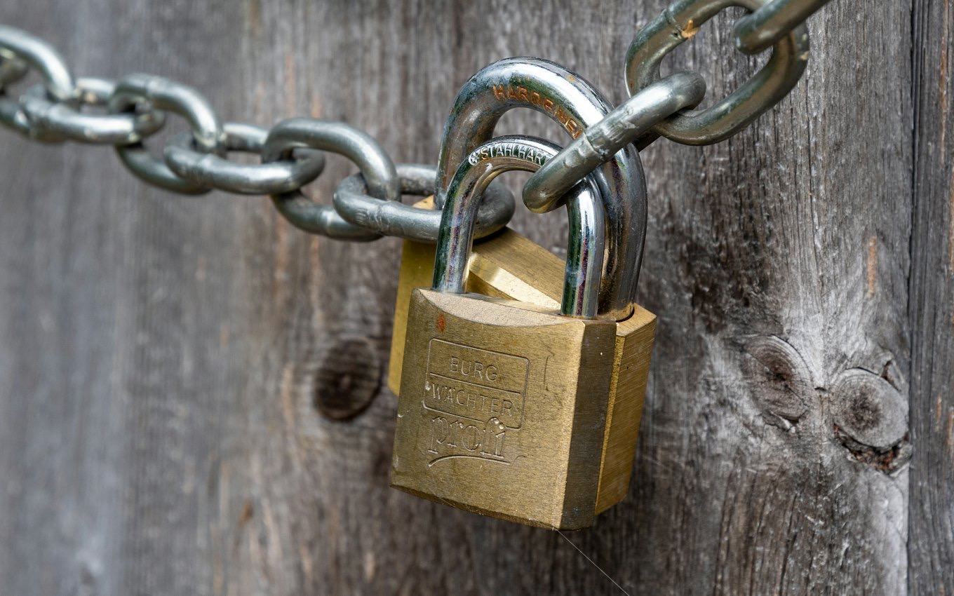A brass padlock on a chain against weathered wood