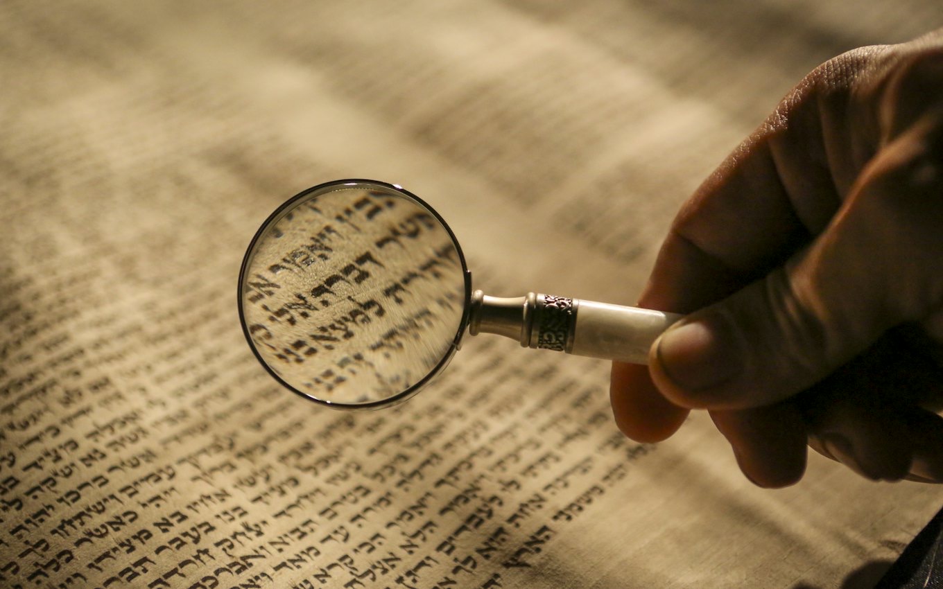 A hand holding a magnifying glass over printed text
