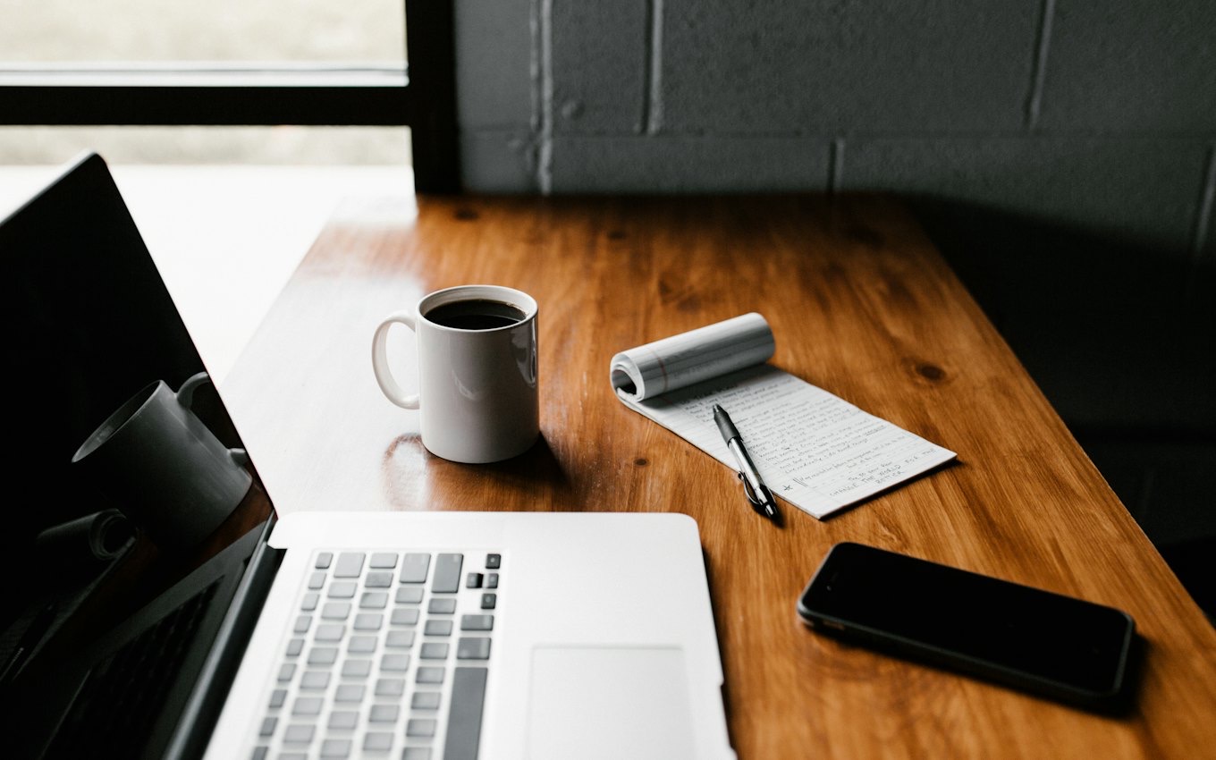 A laptop, a coffee mug and a phone on a wooden desk