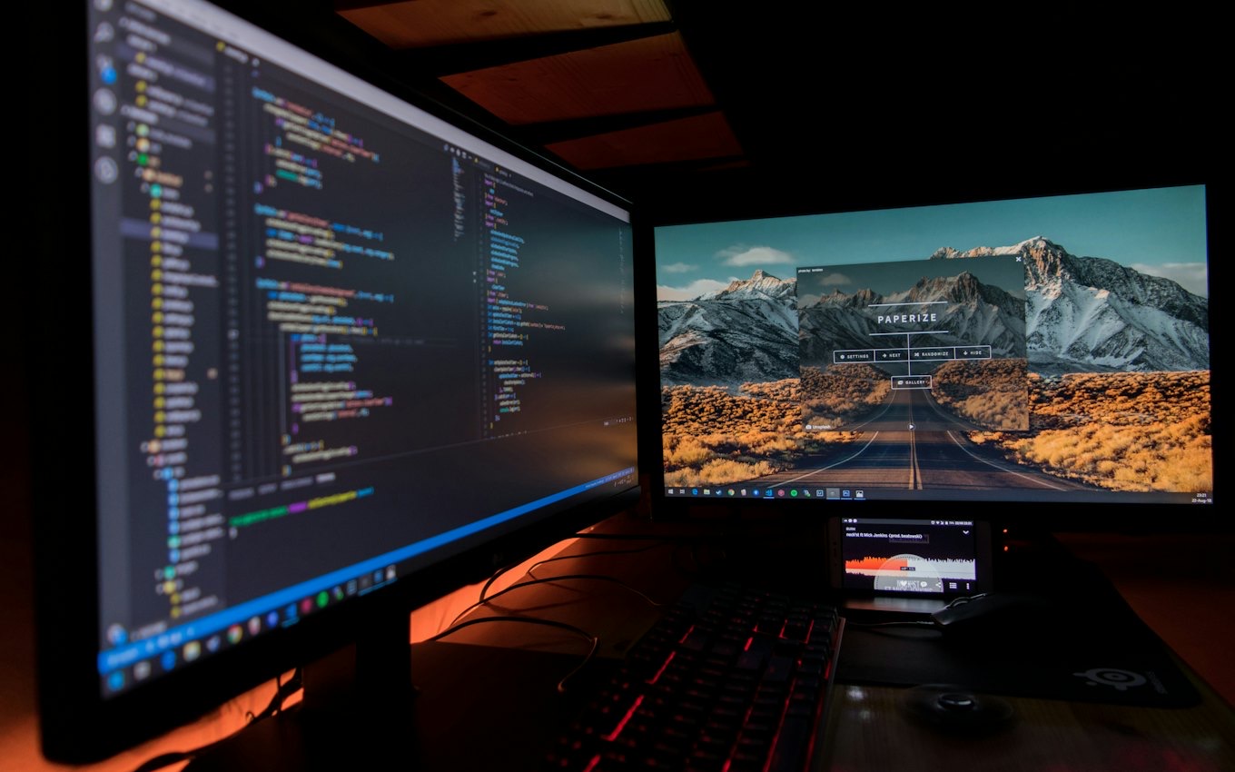 Two monitors showing code in a darkened workspace